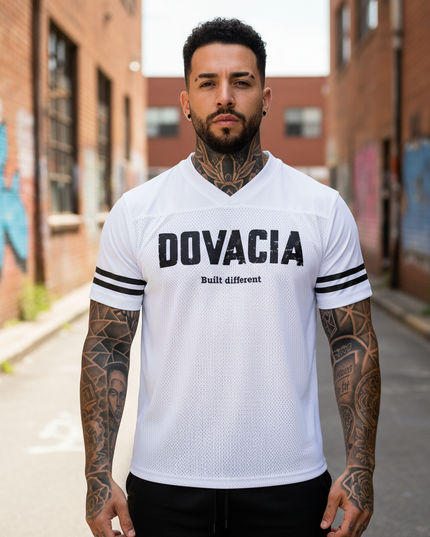 Man wearing a white 'DOVACIA' jersey with tattoos on arms in an urban setting