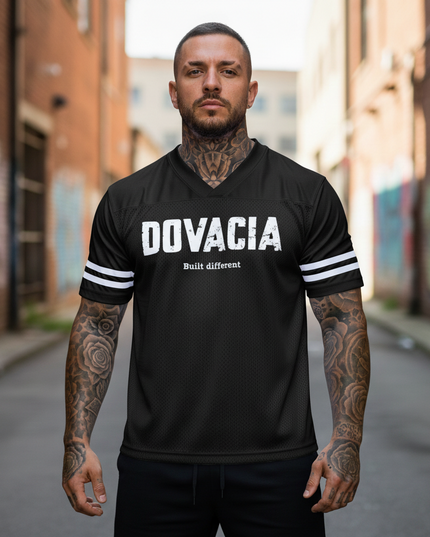 Man wearing a black 'DOVACIA' t-shirt with tattoos on arms standing in an urban setting.