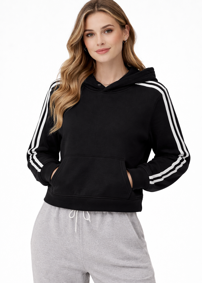 Woman wearing a black hoodie with white stripes on sleeves and gray pants against a white background