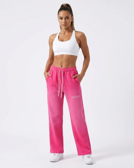 Woman wearing pink sweatpants with a brand logo on a white background