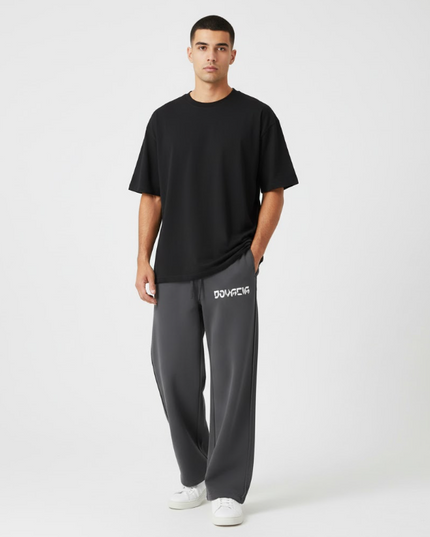 Man wearing a black t-shirt and gray pants with a brand logo on a white background